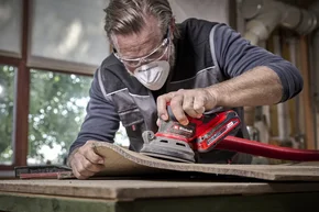 Person schleift Holz mit einem Schwingschleifer.